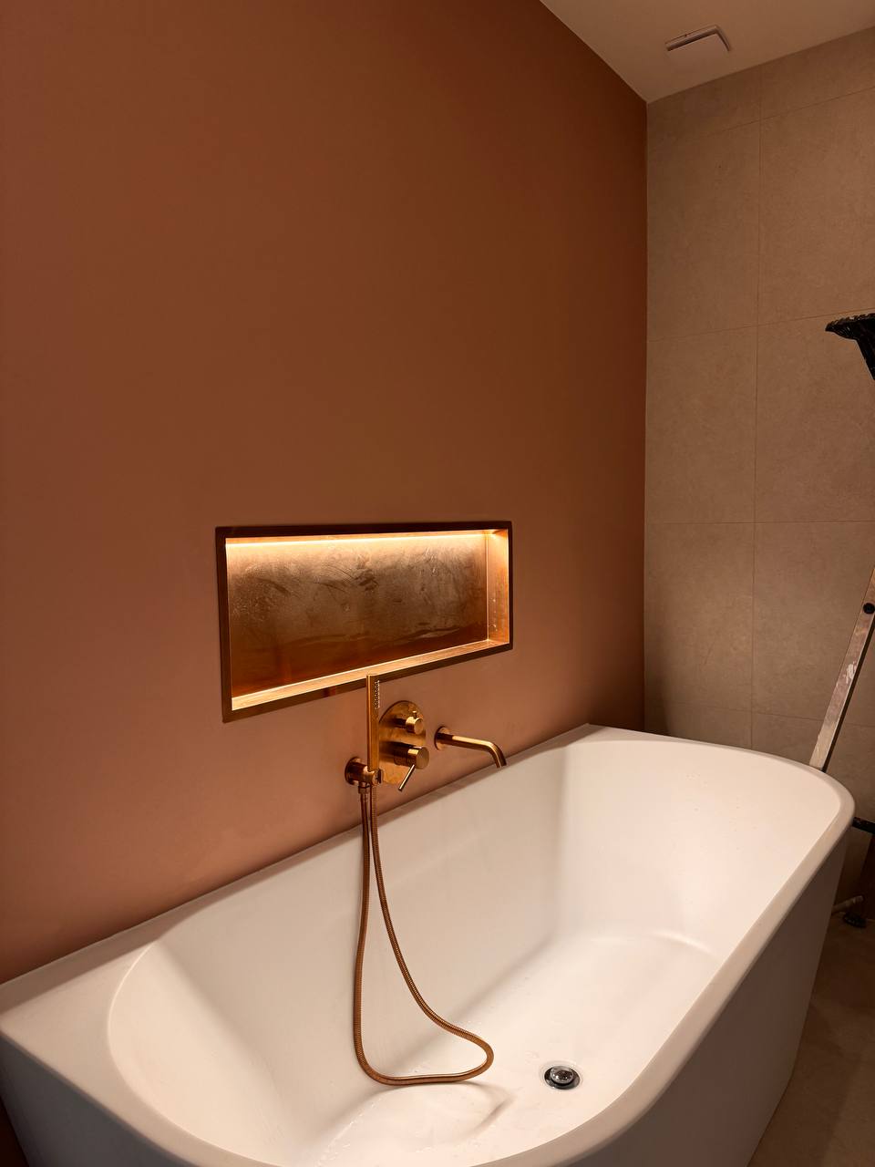 Wit bad met een verlichte wandnis en messingkleurige kraan