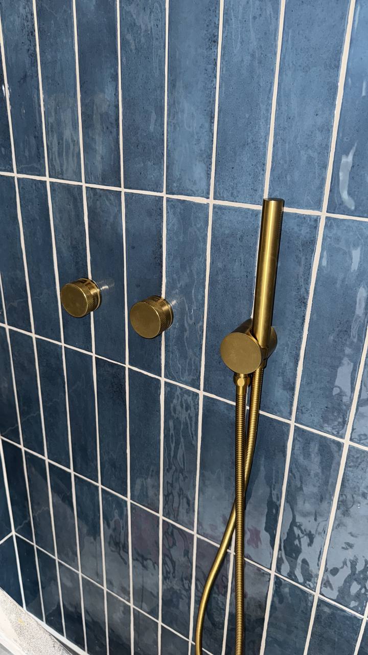 Detail van messingkleurige handdouche op blauwe tegels