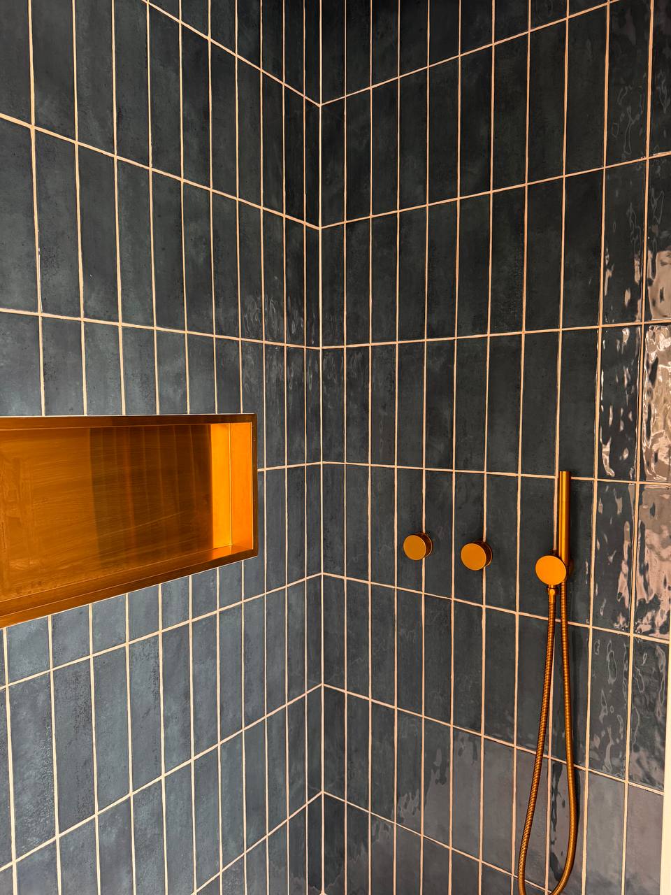 Blauwe verticale douchetegels met messingkleurige inbouwkranen en nis